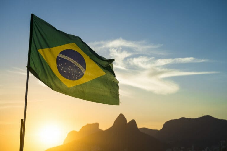 Brazilian flag waving backlit in front of the golden sunset mountain skyline at Ipanema Beach in Rio de Janeiro, Brazil